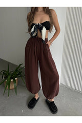 Kahverengi pamuklu müslin şalvar pantolon rahat bir görünüm sunuyor, geniş kesim ve elastik bel detayıyla tasarlandı.