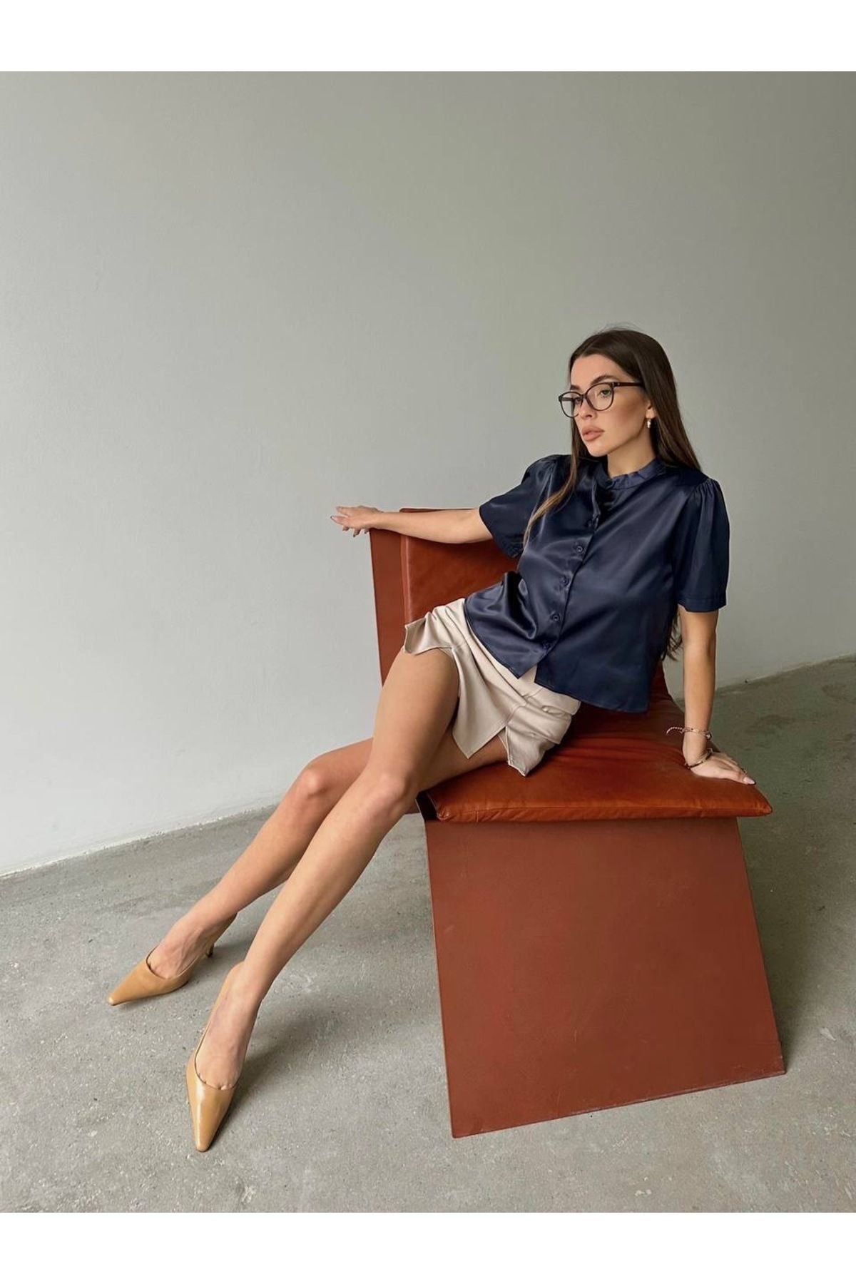 Aec Prive kadın saten kısa kollu gömlek ile şık bir görünüm sergileyen model, rahat bir oturuş pozisyonda.