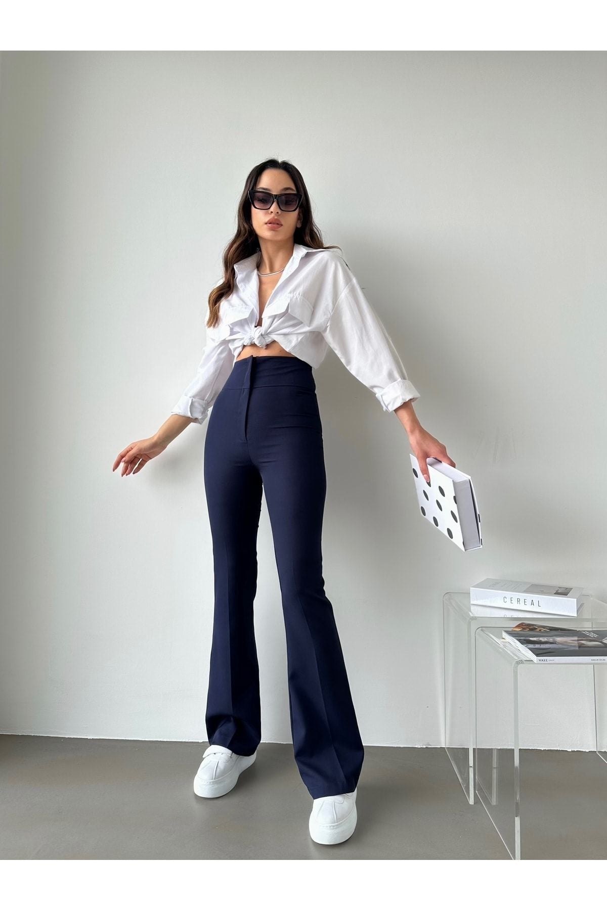 Kadın yüksek bel ispanyol paça pantolon, şık beyaz bluz ve spor ayakkabıyla kombinlenmiş