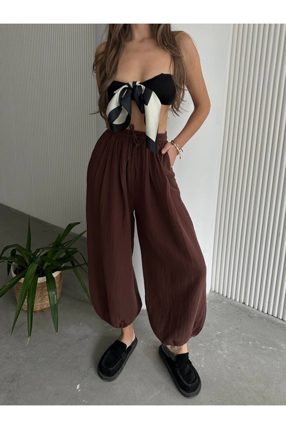 Kahverengi pamuklu müslin şalvar pantolon rahat bir görünüm sunuyor, geniş kesim ve elastik bel detayıyla tasarlandı.